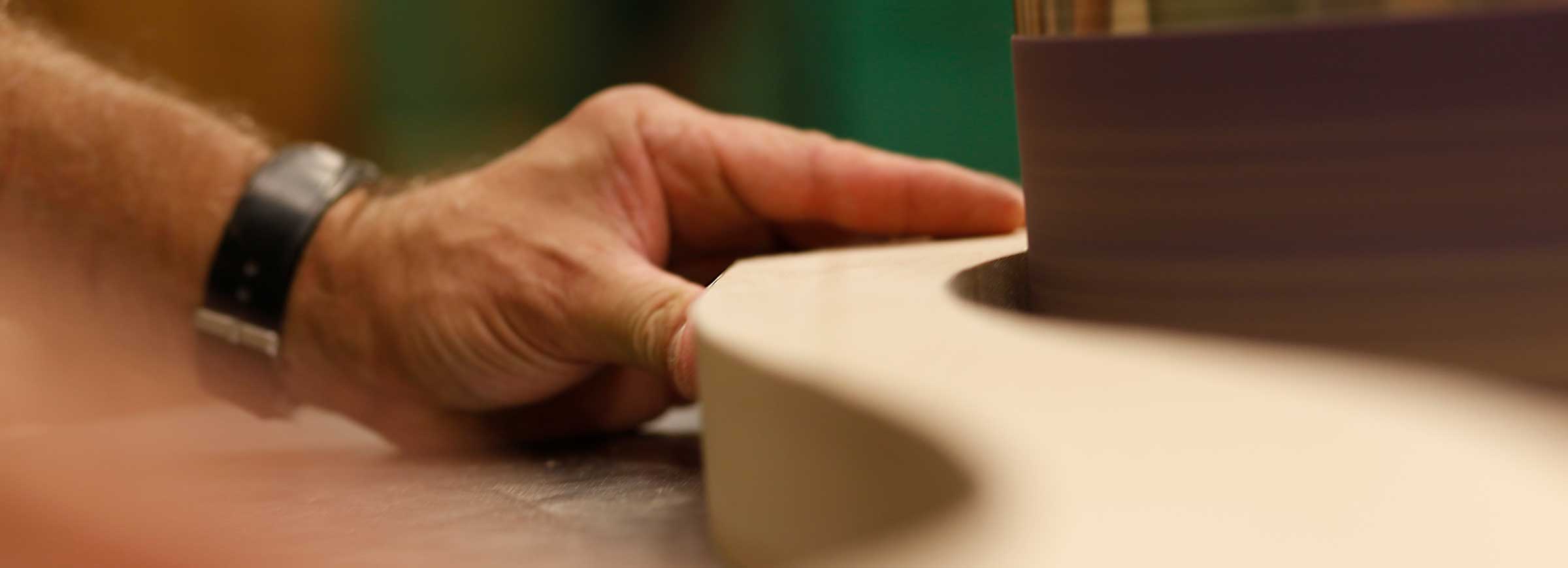 Close up of hands shaping solid wood for a dining table