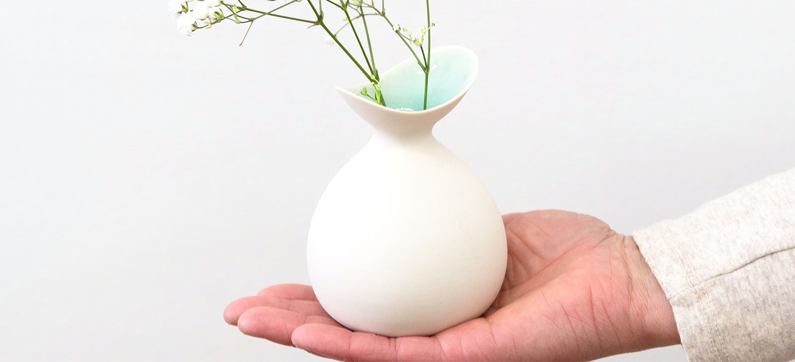 a small sweet white bud vase in the palm of someone's  hand