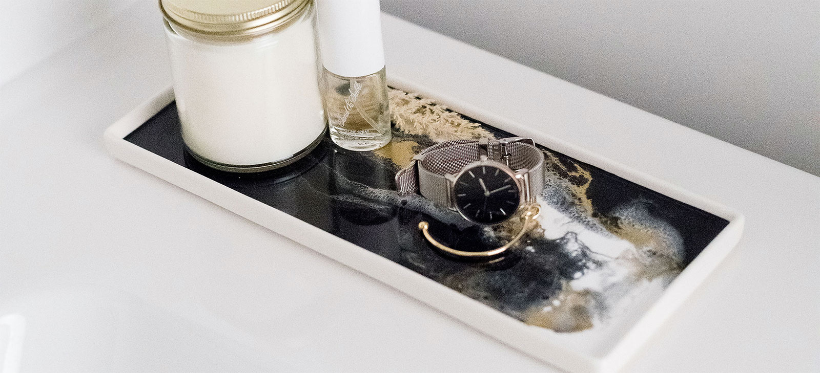 a ceramic and resin tray with perfume, jewelry and a watch