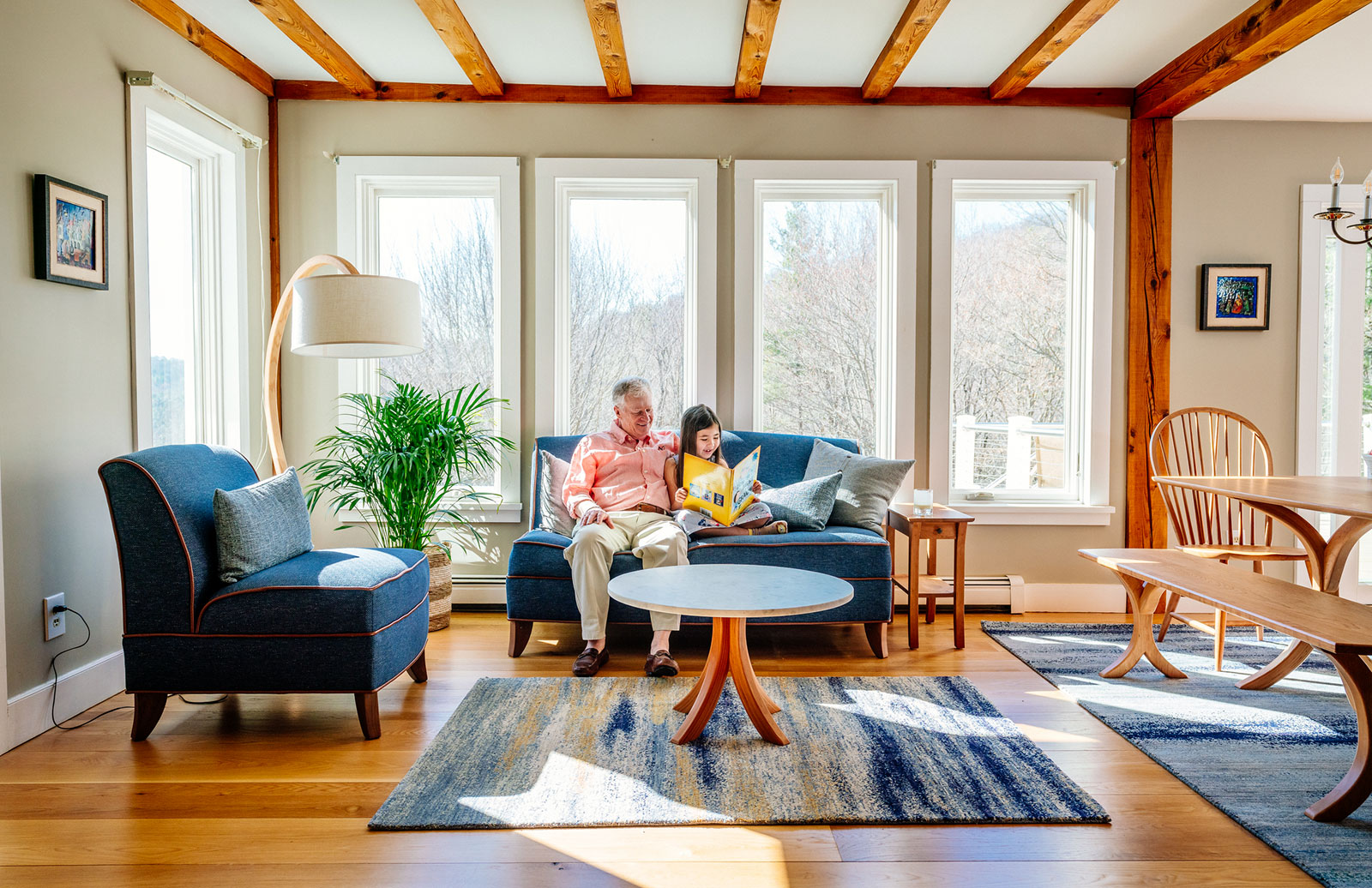 grandfather and granddaughter reading in modern living room on blue couch