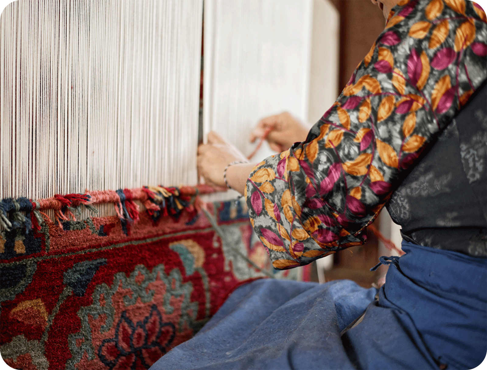 a woman in bright clothing weaving a rug