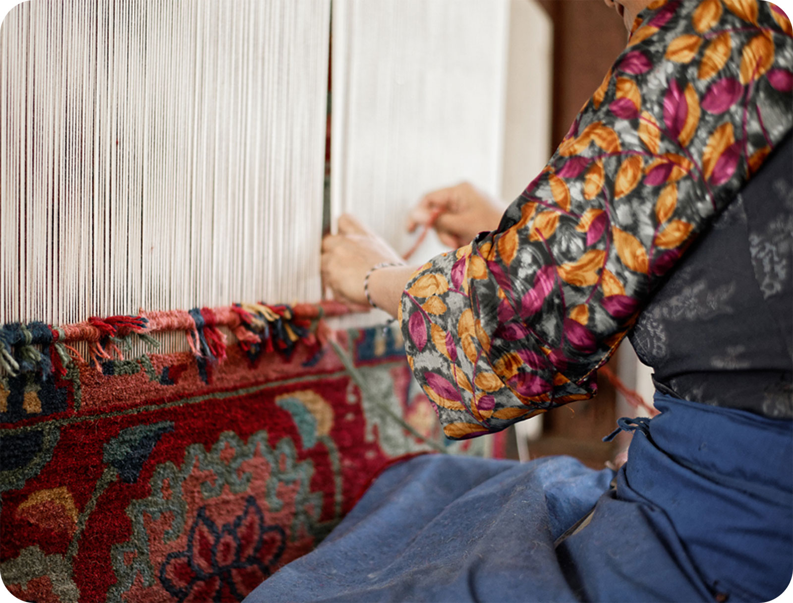 a woman in bright clothing weaving a rug